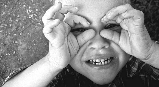 grayscale photography of toddler boy making hand mask thumbnail