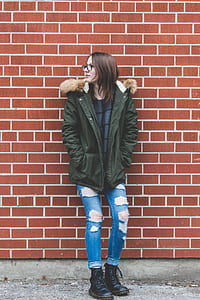 woman leaning against brown bricked wall looking right thumbnail