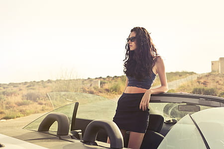 Young Woman In Black Miniskirt And Sunglasses Standing In Convertible Car thumbnail