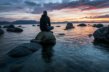 man sitting on gray rock during sunset thumbnail