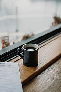 black ceramic coffee mug filled with coffee on window shelf thumbnail