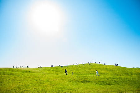 people walking around a green grass hill thumbnail