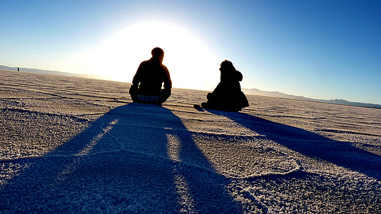man and woman sitting on desert against the sun thumbnail