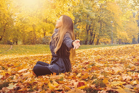 Young woman sitting on a fallen autumn leaves in a park thumbnail