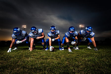 Football Players in Blue Jersey Lined Under Grey White Cloudy Sky during Sunset thumbnail
