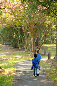 two boys walking on gray soil near green leafed trees during daytime thumbnail