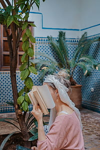 woman covering face with book near plant thumbnail