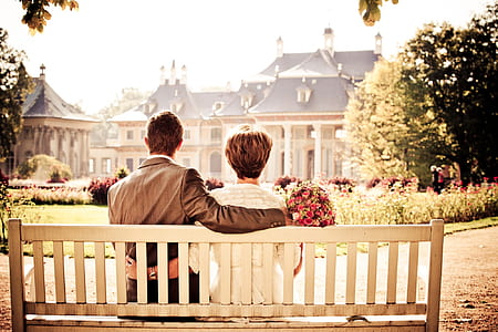 man and woman sits on white wooden outdoor bench in front of white and black house at daytime thumbnail