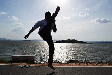 man raising his foot in the middle of the road near body of water thumbnail