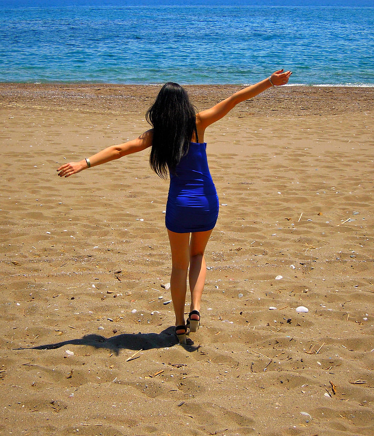 woman wearing blue sleeveless top opening both hands walking towards sea