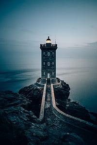 lighthouse on rocky mountain near body of water thumbnail