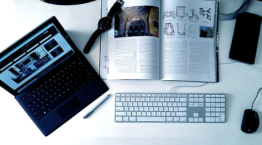 laptop beside book with watch on top next to corded keyboard and computer mouse thumbnail