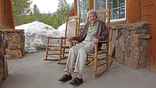woman in green shirt and gray pants with brown cardigan sitting on brown wooden rocking chair thumbnail