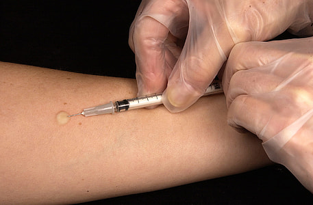 person holding syringe wearing gray surgical gloves covered by dark surface thumbnail