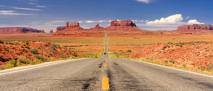 gray concrete road in between grass plains under blue sky at daytime thumbnail