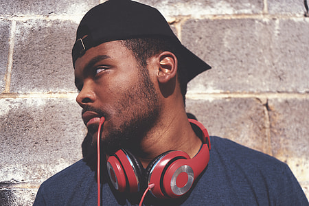 men's wearing cap leaning on wall with red headphones on neck thumbnail