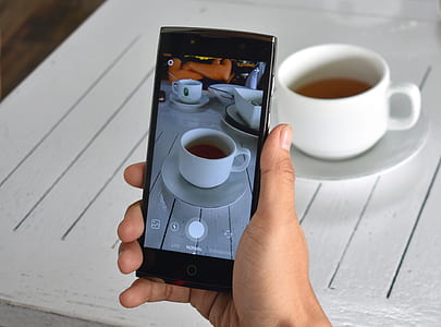 person holding smartphone taking white ceramic teacup on table thumbnail