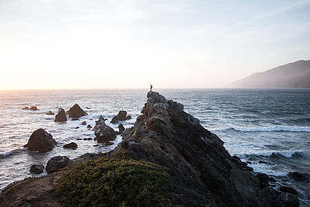 person standing on top of mountain near body of water during daytime thumbnail