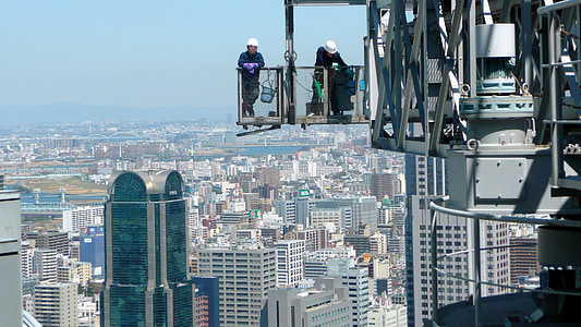 two construction workers standing on crane on top of building thumbnail
