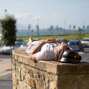 man lying above brown concrete wall near vehicle parking lot during daytime thumbnail