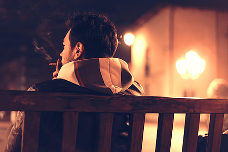 man smoking wearing black and white hoodie sitting on brown wooden bench thumbnail