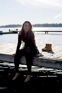 smiling woman sitting on brown wooden deck beside brown work boots at daytime thumbnail