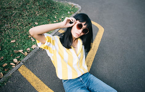 woman in white and yellow striped dress shirt sitting on asphalt road during daytime thumbnail