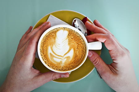 A coffee cup held by hands with a spoon and a paper napkin placed on a saucer thumbnail