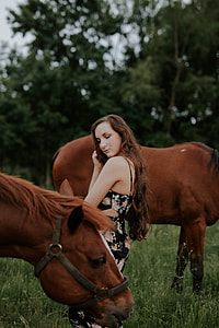 woman standing between two brown horses on green grass field thumbnail
