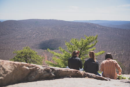 three women sitting on pavement with brown mountains background at daytime thumbnail