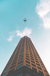 white airliner flying over brown high rise building during daytime thumbnail