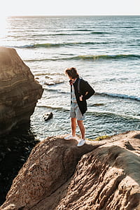 man standing on rock formation near sea thumbnail