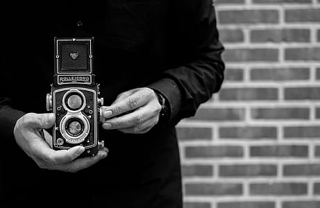 grayscale photo of person holding double lens camera thumbnail