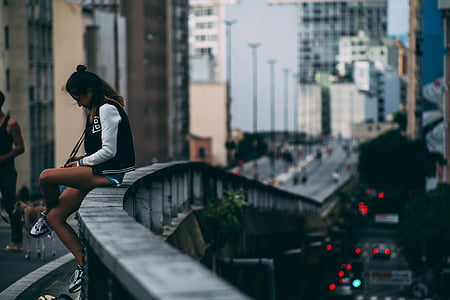 selective focus photo of woman sitting on gray concrete rail near building at daytime thumbnail