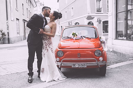 new wedding couple kissing at side of red car thumbnail