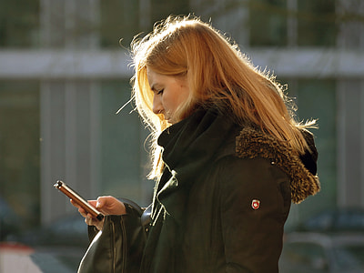 selective focus photography of woman standing near building while using smartphone thumbnail