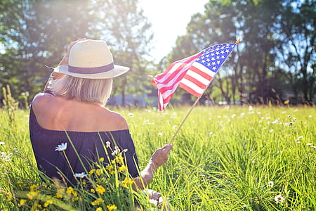 woman holding U.S.A flag sitting on green grass field during daytime thumbnail