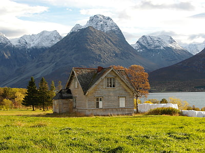 brown wooden house near river and mountain thumbnail