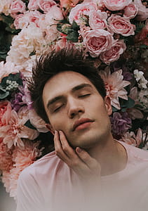 man wearing white crew-neck tee shirt closing both eyes while leaning on assorted light-color flowers thumbnail