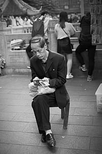 grayscale photography of man sitting on wooden chair thumbnail