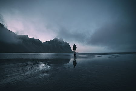 silhouette of man standing on the shore with dark clouds above thumbnail