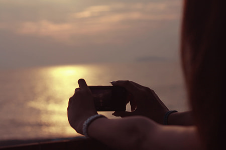 person holding camera taking photo of sea at sunset thumbnail