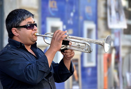 man playing trumpet near blue and gray wall thumbnail