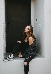 woman in distressed black jeans sits on grey concrete doorway thumbnail