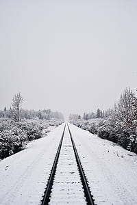 black train railway covered by snow under white sky at daytime thumbnail