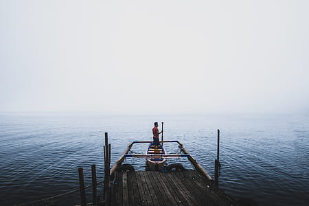 man standing on beige row boat on body of water during daytime thumbnail