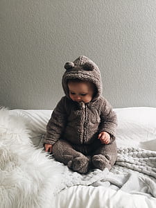 baby's wearing gray onesie sittin on bed thumbnail