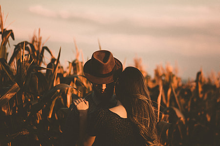man in brown fedora hat hugging woman in black top beside plants thumbnail