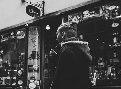 Grayscale Photograph of Man Walking Past by Shop thumbnail