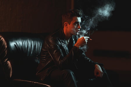 man holding cigarette stick while sitting on chair thumbnail